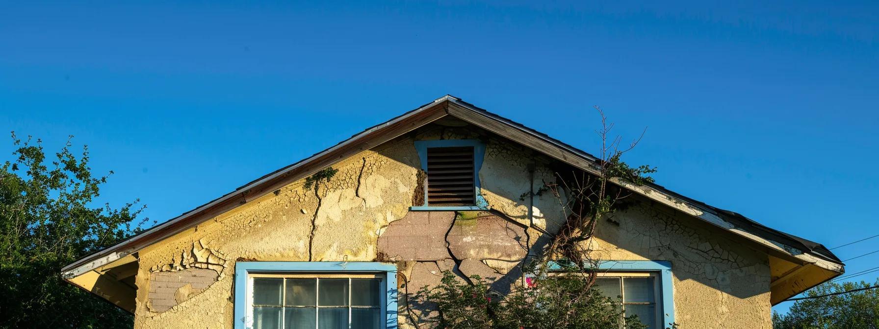 a distressed suburban san antonio home showcases visible cracks in the exterior walls and a sagging porch, set against a clear blue sky, highlighting the urgent need for foundation repair.